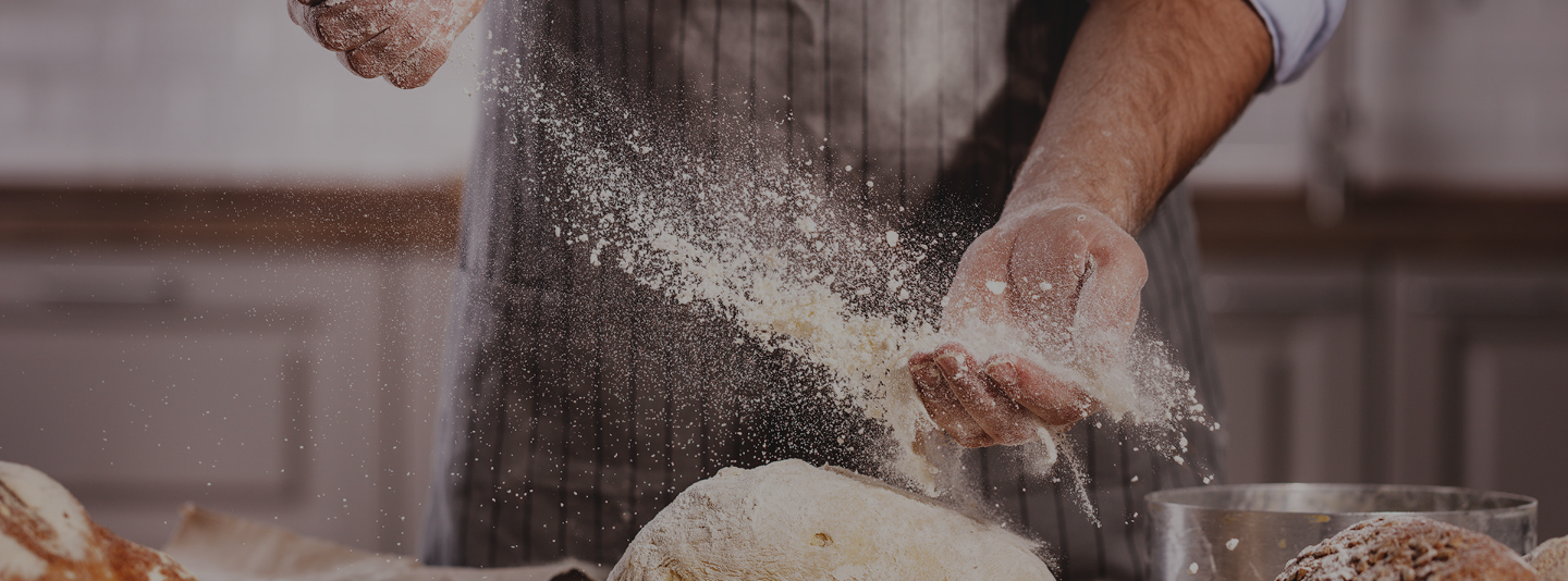 Baking Chef in an apron scattering flour over dough